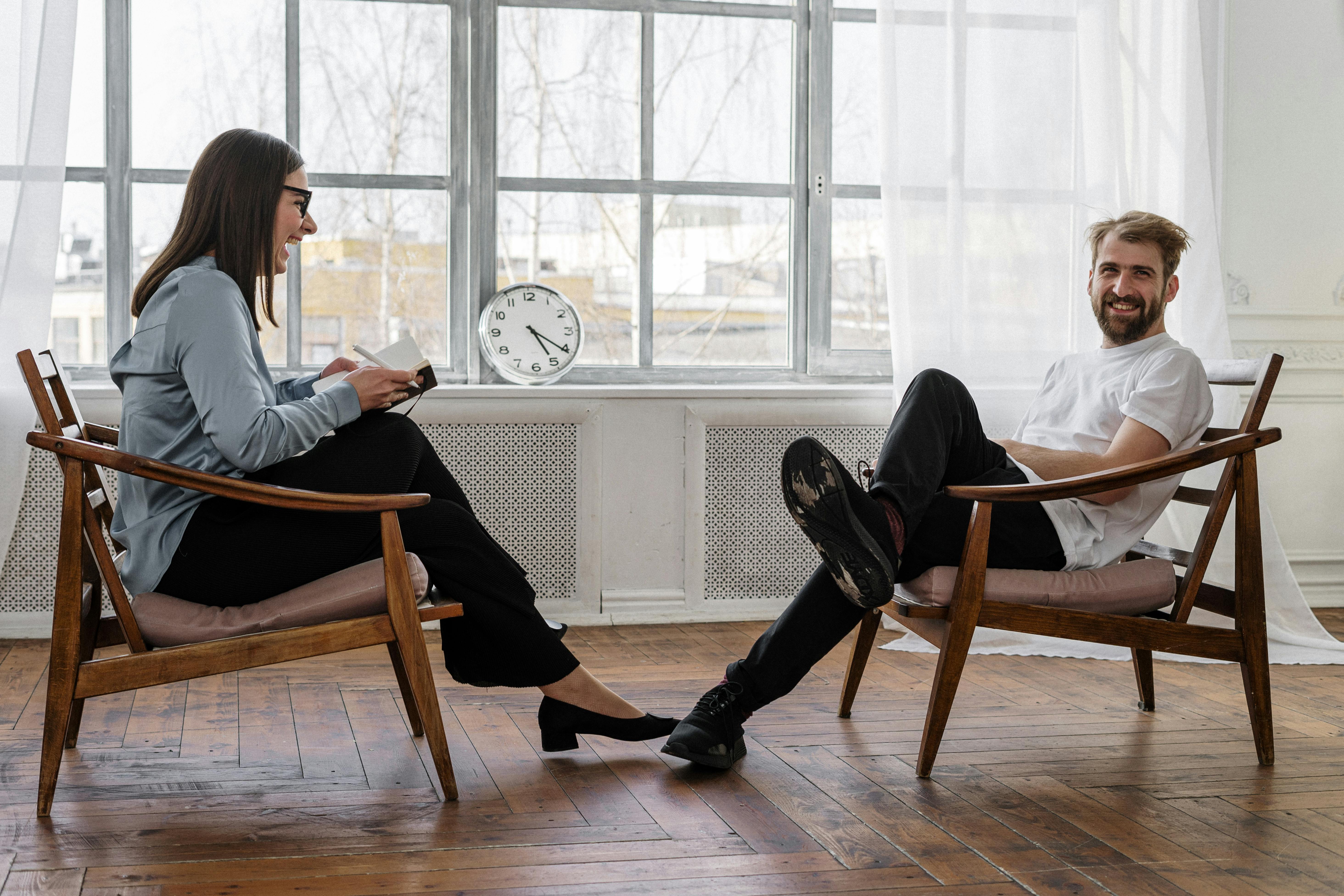 Two people sitting in chairs, facing each other and laughing